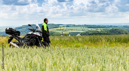 Adventure motorcycle and biker man traveling, standing and watching the landscape. Freedom travel lifestyle in Germany, Europe.