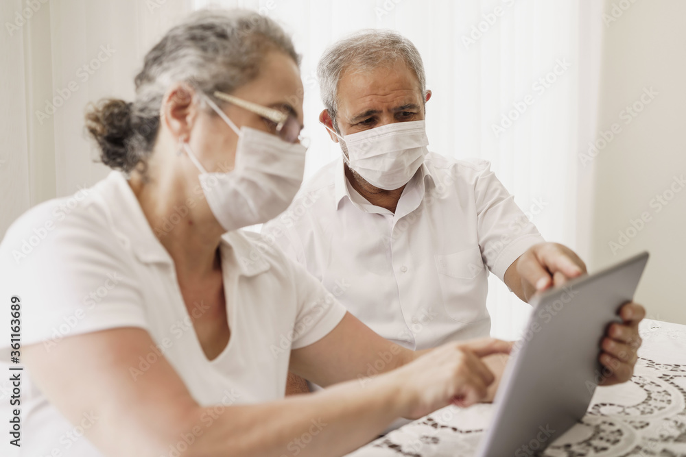 Senior couple wearing medical face mask and using tablet at home. quarantine. Corona Virus. order of products online and communicates on the Internet at home. stay home concept