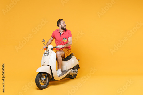 Cheerful young bearded man guy in casual summer clothes driving moped isolated on yellow wall background studio portrait. Driving motorbike transportation concept. Mock up copy space. Looking aside. © ViDi Studio