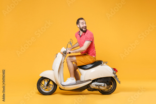 Side view of excited young bearded man guy in casual summer clothes driving moped isolated on yellow background in studio. Driving motorbike transportation concept. Mock up copy space. Looking aside. © ViDi Studio