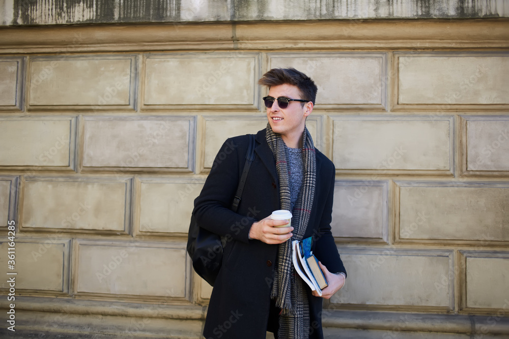Stylish male student with books and takeaway coffee on street