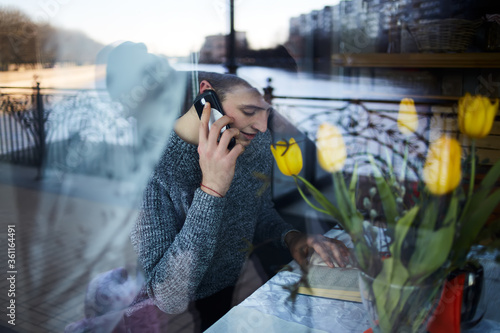 Happy man talking on smartphone and reading book in cafe