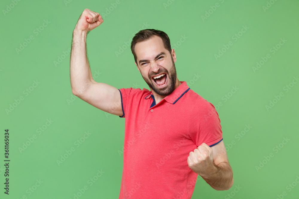 Joyful young bearded man guy in casual red pink t-shirt posing isolated on green background studio portrait. People sincere emotions lifestyle concept. Mock up copy space. Clenching fists like winner. Joyful young bearded man guy in casual red pink t-shirt posing isolated on green background studio portrait. People sincere emotions lifestyle concept. Mock up copy space. Clenching fists like winner.
