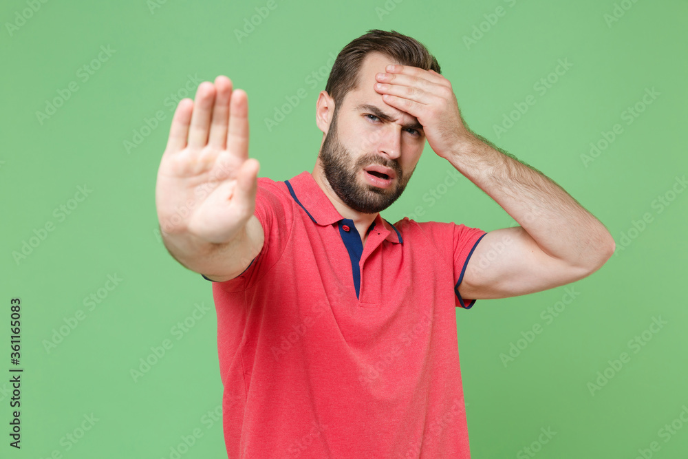 Displeased young bearded man guy in casual red pink t-shirt posing isolated on green background studio. People lifestyle concept. Mock up copy space. Showing stop gesture with palm, put hand on head. Displeased young bearded man guy in casual red pink t-shirt posing isolated on green background studio. People lifestyle concept. Mock up copy space. Showing stop gesture with palm, put hand on head.