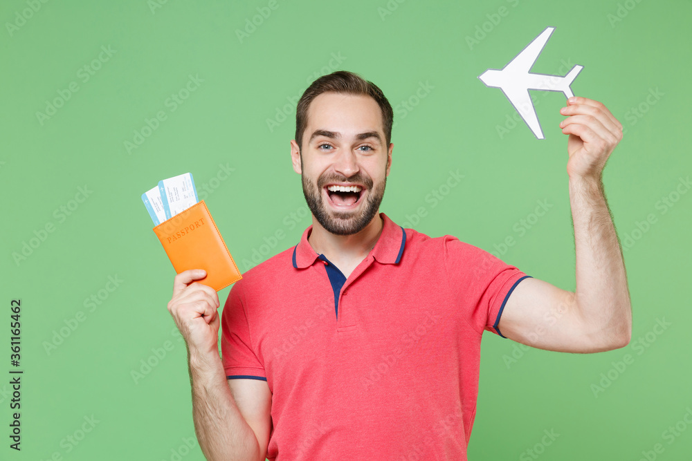Cheerful young bearded man guy in red pink t-shirt isolated on green background. Passenger traveling abroad to travel on weekends getaway. Air flight journey concept. Hold passport tickets air plane. Cheerful young bearded man guy in red pink t-shirt isolated on green background. Passenger traveling abroad to travel on weekends getaway. Air flight journey concept. Hold passport tickets air plane.