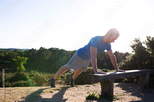 man doing press ups on a bench in the countryside