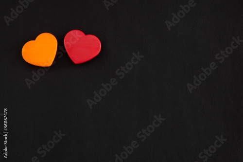 Two red and orange color hearts lying close together isolated at the top left corner of black paper background. Flat lay with empty space for text.