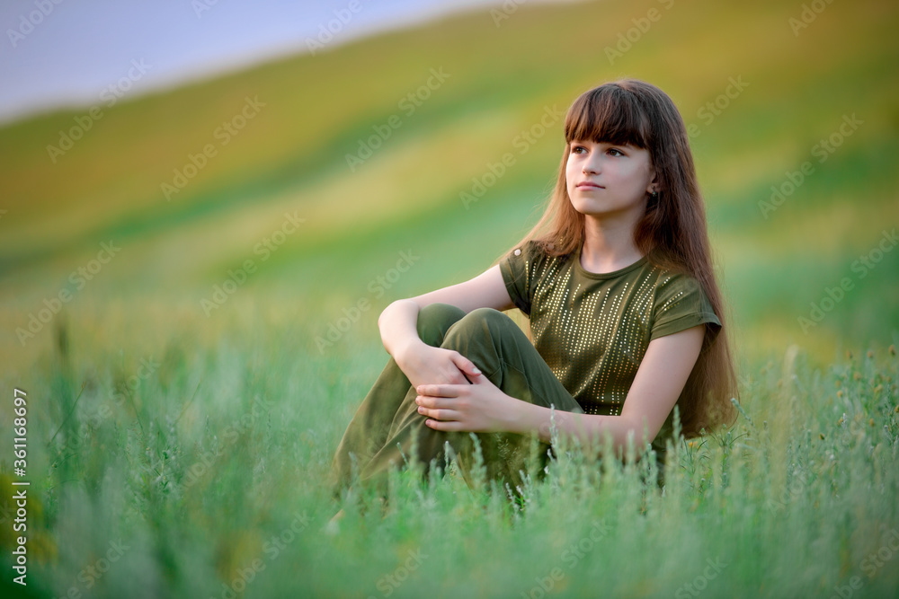 Portrait of a girl with long flowing hair at sunset. Street photography. Green-eyed beautiful girl. Girl sitting in the tall grass. Portrait of a girl with long flowing hair at sunset. Street photography. Green-eyed beautiful girl. Girl sitting in the tall grass.