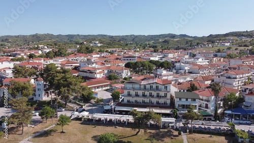 Chalkidiki, Greece coastal village landscape drone shot. Aerial view of Hanioti or Chaniotis at Kassandra peninsula with panning from tavern restaurants to low rise buildings with red tiled roofs. photo