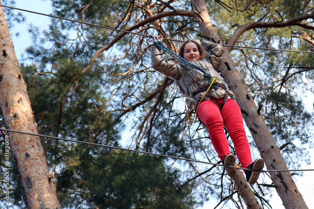 Fototapeta premium Overcoming obstacles. Little girl climbing on a rope in adventure park