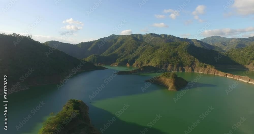 Overhead view of pristine green calm water and sunlight on green mountains on bright blue sunny sky day, Jiguey Dam, Dominican Republic, above aerial approach Overhead view of pristine green calm water and sunlight on green mountains on bright blue sunny sky day, Jiguey Dam, Dominican Republic, above aerial approach