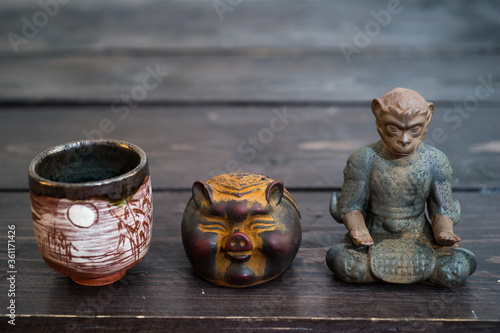 Different tea decorative chinese figurines: king of monkey, pig and tea bowl on dark wooden table