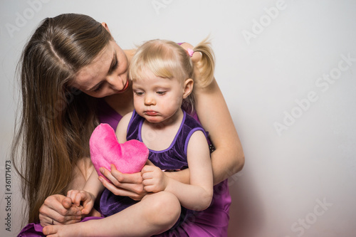 Mother consoles her sad daughter and gives her a pink plush heart on light gray background