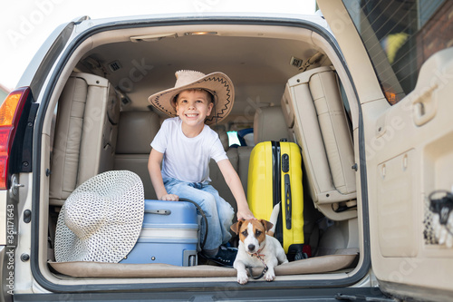 Happy boy in a cowboy hat and puppy jack russell terrier travel by car. A child and a funny little dog are sitting in the trunk and are ready for summer vacation. Independent travel. Best friends. photo