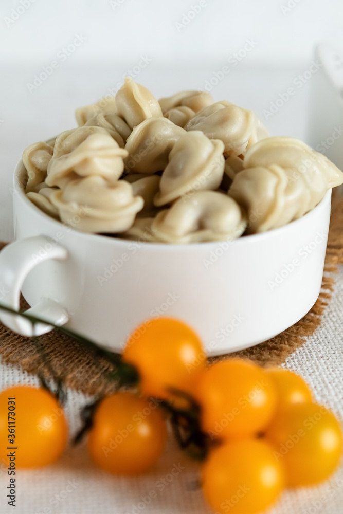 Composition on a light background, a Cup with ravioli dumplings with meat filling and cherry tomatoes. The concept of cooking delicious food at home. Selective focus. Composition on a light background, a Cup with ravioli dumplings with meat filling and cherry tomatoes. The concept of cooking delicious food at home. Selective focus.