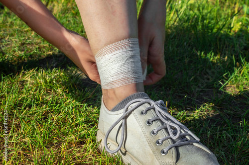 Ankle sprain, woman bandages her leg while walking on a summer nature. Concept of tired legs, injury on running