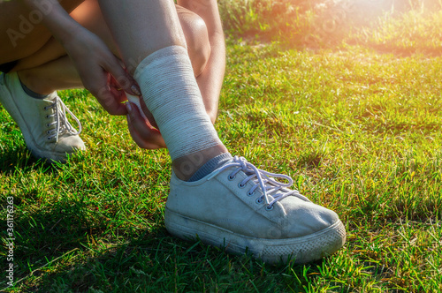 Young woman runner bandages her legs to protect tendons during long run and physical activity. Evening workout outdoors in the park