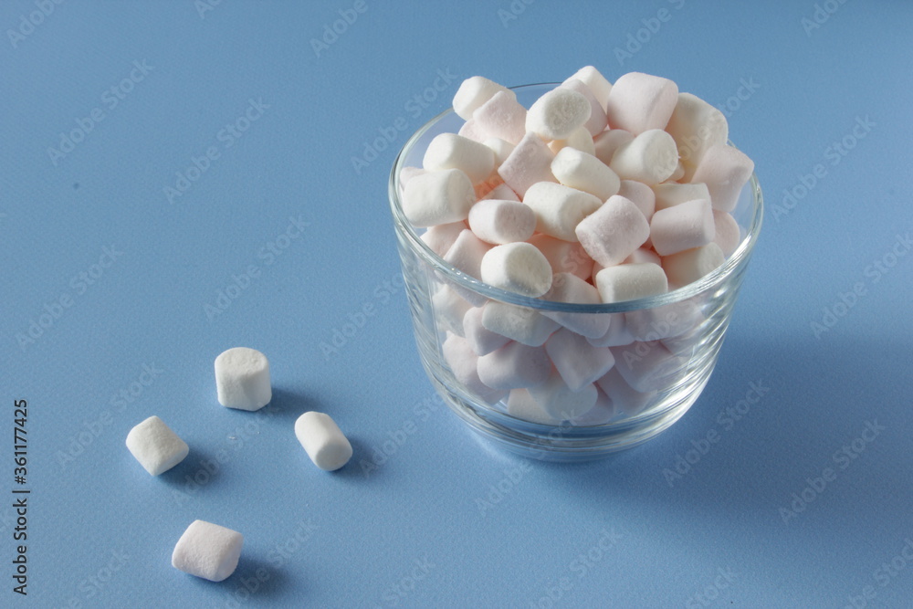 White Fluffy marshmallows in white cup isolated on blue background. Mini marshmallows. Winter food background concept. White Fluffy marshmallows in white cup isolated on blue background. Mini marshmallows. Winter food background concept.