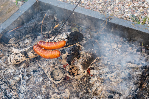 Roasting sausages in the garden bonfire. Barbeque grill fireplace.
