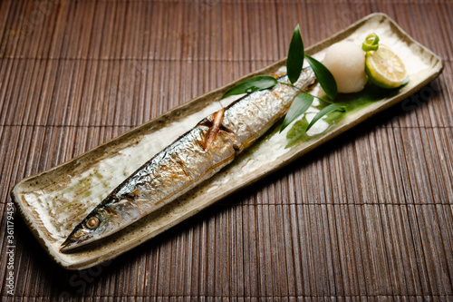 grilled whole mackerel fish with lime citrus and grated daikon radish on a long rectangler plate on bamboo table mat