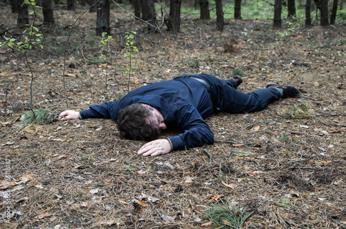 Murder in the woods. The body of a man in a blue shirt and trousers lies on the ground among the trees in the forest. Victim of an attack.