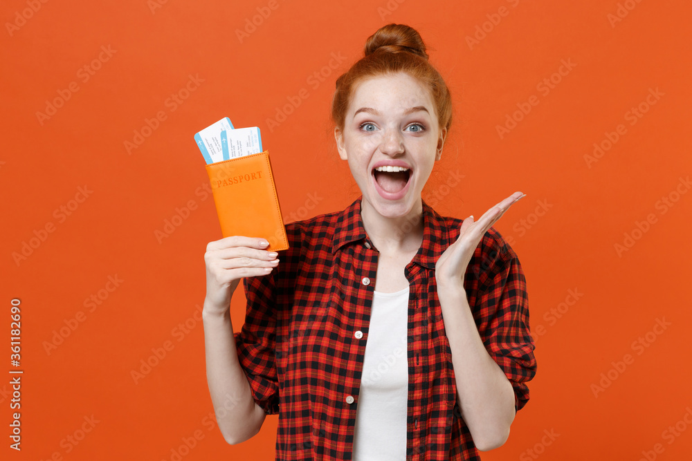 Excited young girl in red checkered shirt isolated on orange background. Passenger traveling abroad to travel on weekends getaway. Air flight journey concept. Hold passport tickets spreading hands. Excited young girl in red checkered shirt isolated on orange background. Passenger traveling abroad to travel on weekends getaway. Air flight journey concept. Hold passport tickets spreading hands.