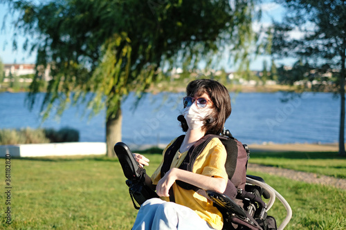 Disabled woman with muscular dystrophy in an electric wheelchair wearing a white face mask for protection during coronavirus outbreak