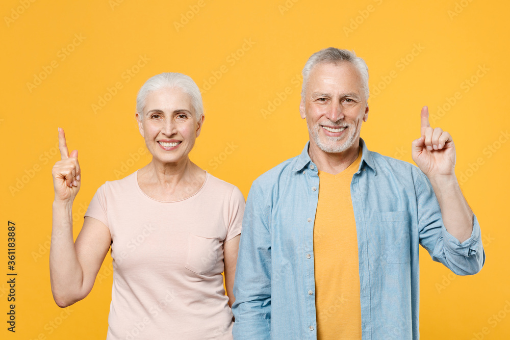 Smiling elderly gray-haired couple woman man in casual clothes posing isolated on yellow background studio portrait. People emotions lifestyle concept. Mock up copy space. Pointing index fingers up. Smiling elderly gray-haired couple woman man in casual clothes posing isolated on yellow background studio portrait. People emotions lifestyle concept. Mock up copy space. Pointing index fingers up.