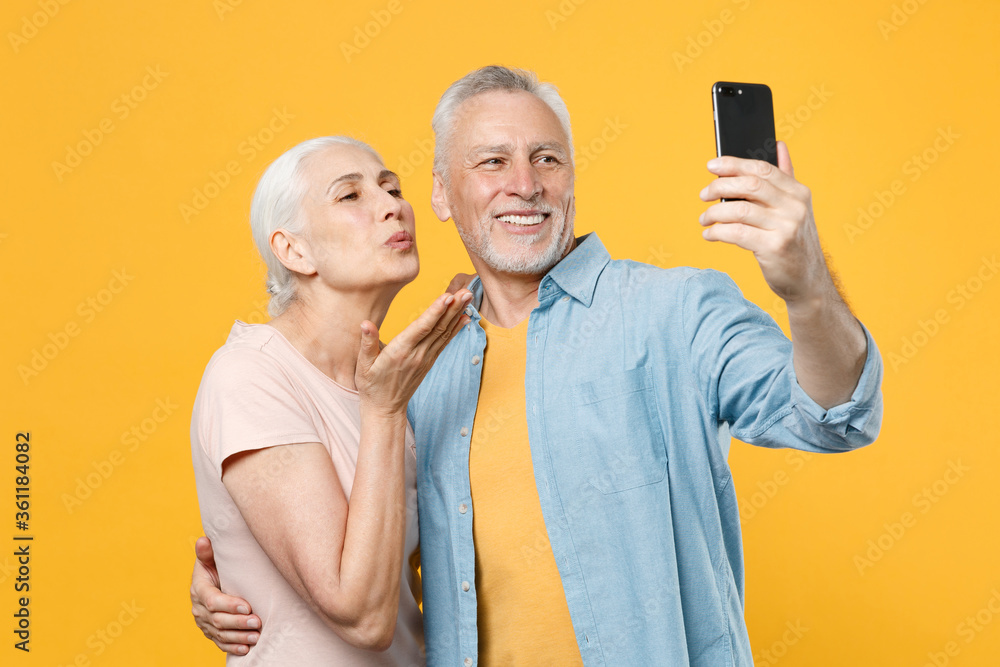Funny elderly gray-haired couple woman man in casual clothes isolated on yellow background. People lifestyle concept. Mock up copy space. Doing selfie shot on mobile phone, blowing sending air kiss. Funny elderly gray-haired couple woman man in casual clothes isolated on yellow background. People lifestyle concept. Mock up copy space. Doing selfie shot on mobile phone, blowing sending air kiss.