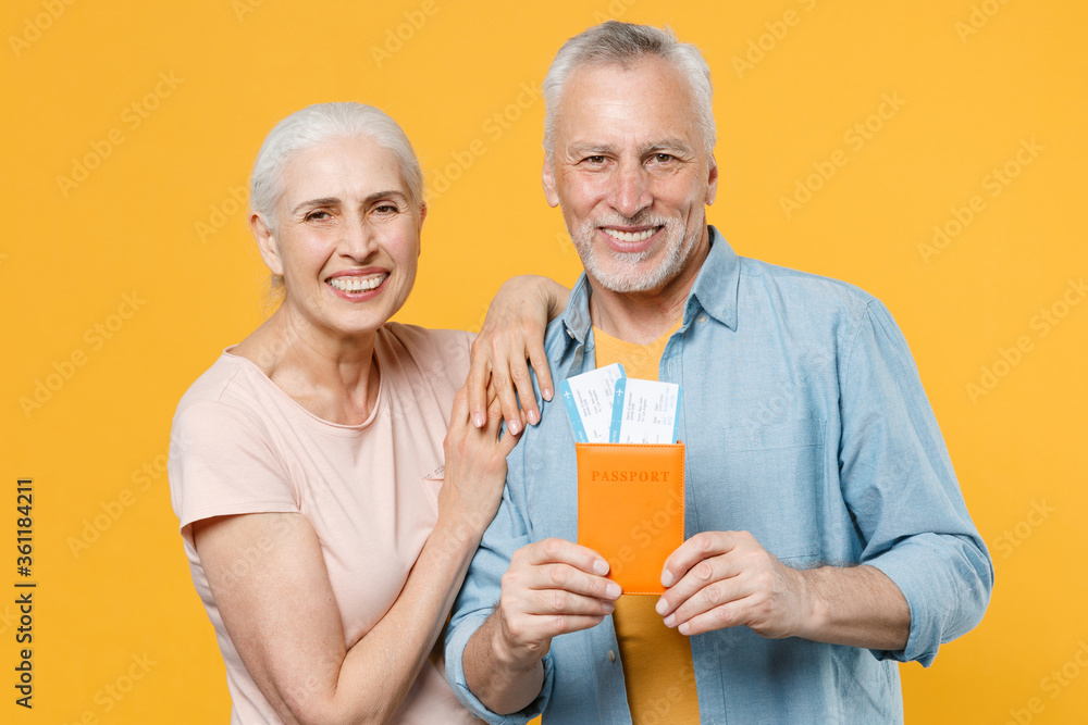 Smiling elderly gray-haired couple woman man in casual clothes isolated on yellow background. Passenger traveling abroad travel on weekends getaway. Air flight journey concept. Hold passport, tickets. Smiling elderly gray-haired couple woman man in casual clothes isolated on yellow background. Passenger traveling abroad travel on weekends getaway. Air flight journey concept. Hold passport, tickets.