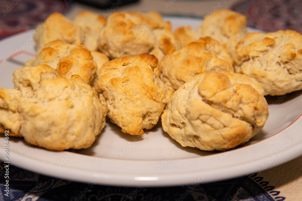 Un plato lleno de scones recien preparados. Puestos sobre una mesa y debajo de una luz calida Un plato lleno de scones recien preparados. Puestos sobre una mesa y debajo de una luz calida