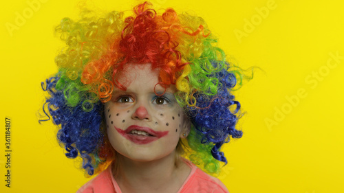 Little child girl clown in colorful wig making silly faces, having fun, smiling, dancing. Halloween