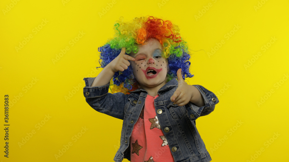 Little child girl clown in colorful wig making silly faces. Having fun, smiling, dancing. Halloween Little child girl clown in colorful wig making silly faces. Having fun, smiling, dancing. Halloween
