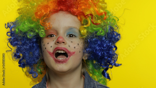 Little child girl clown in colorful wig tells something interesting. Having fun, smiling. Halloween
