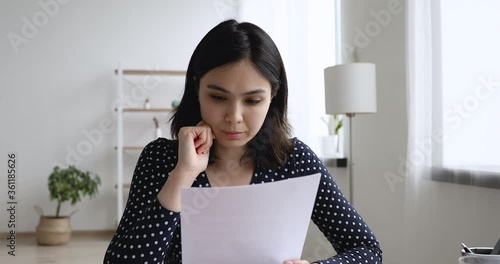 Asian young student girl sit at desk at home prepare essay read report document ponders over amendments feels doubtful insecure about paragraph looks out the window thinking study work process concept