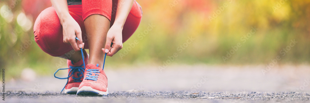 Exercise and sport running shoes runner woman tying laces getting ready for summer run in forest park panoramic banner header crop. Jogging girl exercise motivation heatlhy fit living.