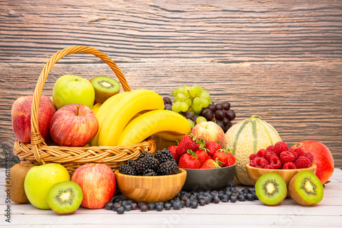 Fototapeta Naklejka Na Ścianę i Meble -  Group Healthy fresh fruit in a wooden basket, With vitamins c from bananas, kiwi, grapes, raspberries, blueberries, and blackberries, good for the body and diet food on the table in nature background.