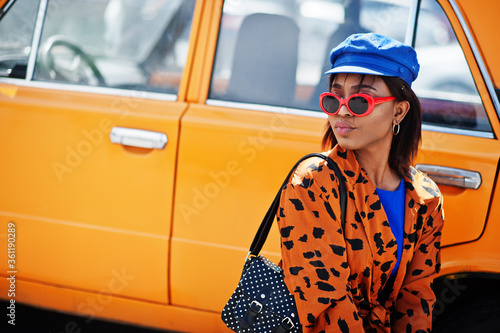 Beautiful african american lady with sunglasses standing near orange classic retro car.