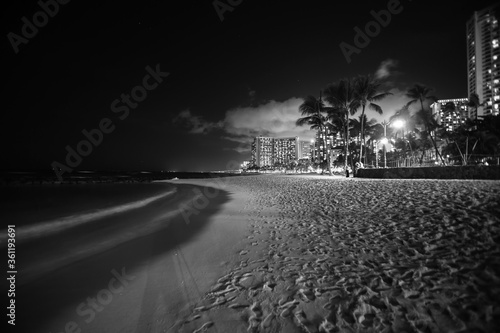 Beach palm trees and buildings of Waikiki from beach on tropical island night