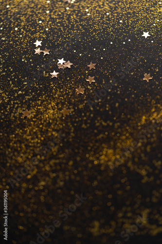 Beautiful Christmas light background. Abstract glitter bokeh and scattered sparkles in gold, on black © neirfy