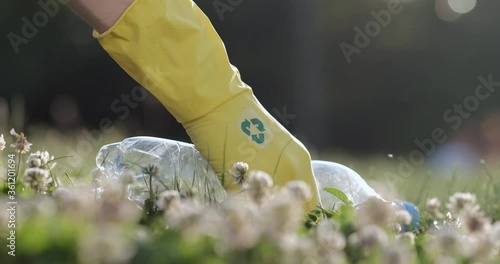 Close up of a plastic bottle, a man raises a plastic bottle with his hand in a yellow glove with a recycle sign.