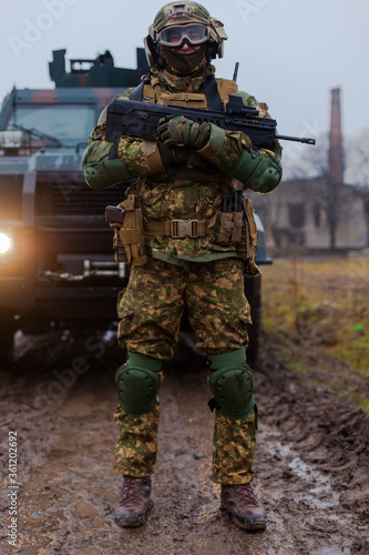 soldier is ready to shoot against the background of an armored car and the included headlights
