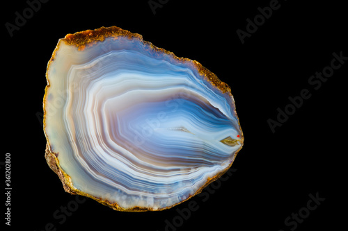 Close-up of polished agate gem with smooth icy surface texture isolated on black background. White-blue cut precious stone from north-east Czechia. Wavy pattern of concentric curves in cross section.