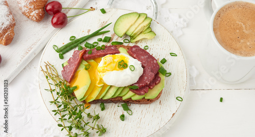 toast with poached egg and avocado on a round board, next to croissants and ripe red cherries