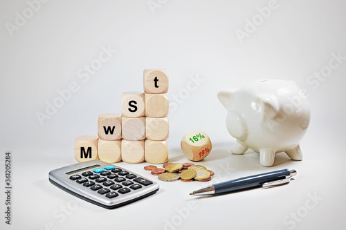 Calculator, piggy bank and dices with German text MwSt (value added tax), reduction from 19% to 16%, economic stimulus package in the coronavirus crisis, gray background, copy space photo