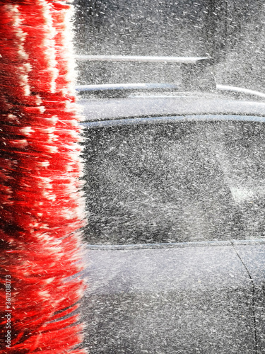 Car wash with red brush roller that sprinkles water droplets. Professional car washing cleaning business concept.