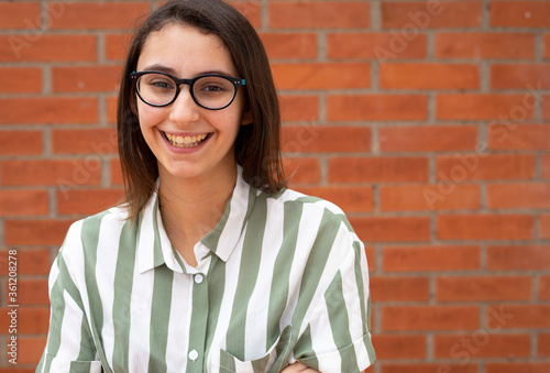 Tableau sur toile Business woman in glasses and striped shirt smiling at a brick wall