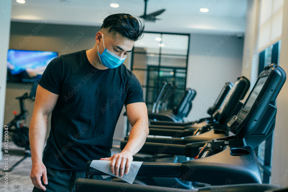 young asian male wearing mask, cleaning treadmill with sanitizing wipe COVID19 young asian male wearing mask, cleaning treadmill with sanitizing wipe COVID19