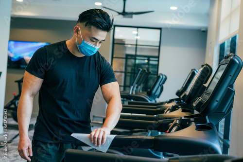 Fotografie Asian male wearing mask during COVID19 wiping down treadmill