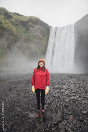 Iceland landscape photo of brave girl who proudly standing with his arms raised in front of water wall of mighty waterfall.